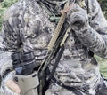 Tan braided JAKT GEAR binocular sling worn across a camouflage jacket, carrying binoculars at the hunter’s side.